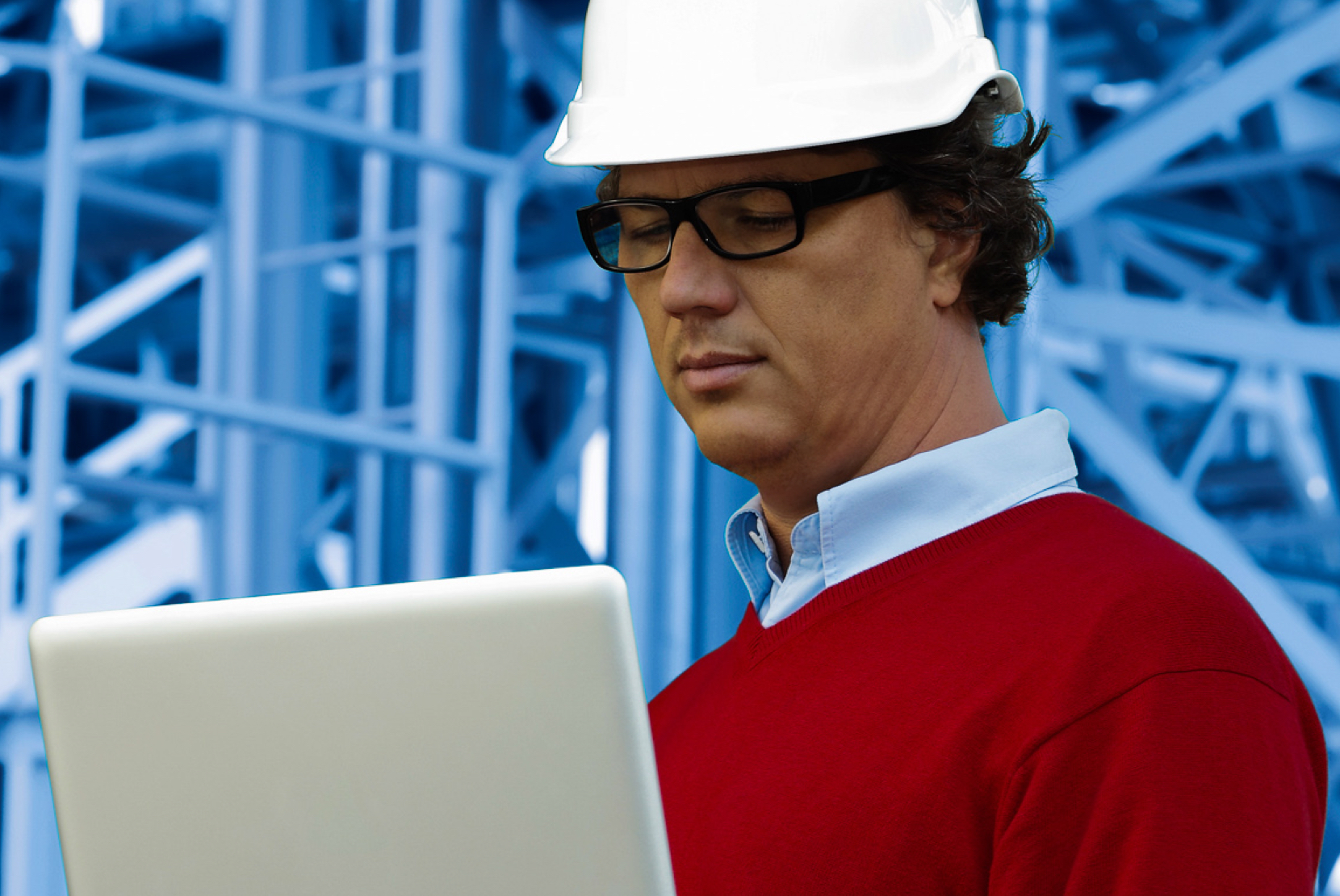 Image of a frontline worker wearing a white hard hat and using a laptop in the plant environment